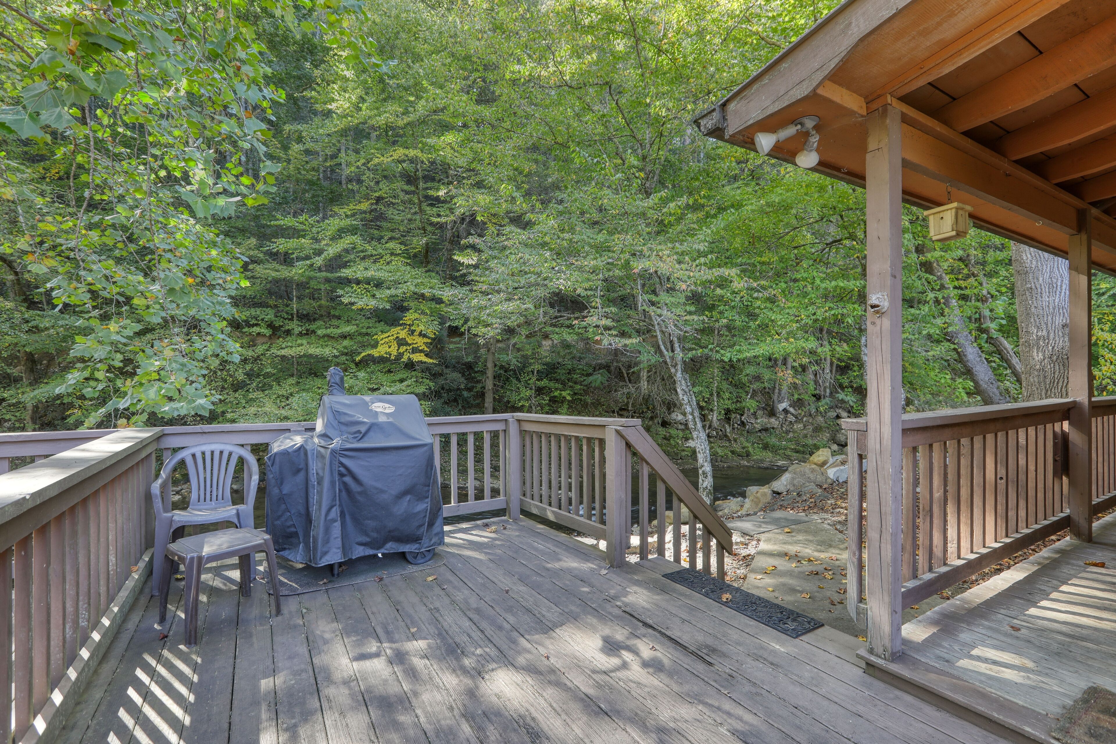 A wooden deck with a covered grill area, a chair, and a view of a forested area.