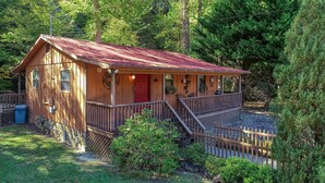 A wooden cabin with a red door, a porch, and a small staircase leading to a deck.