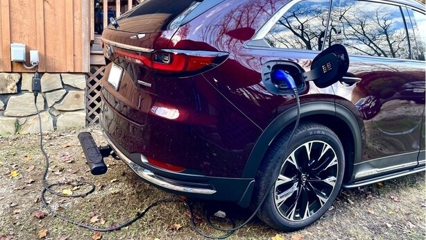 A maroon SUV parked outdoors with a charging cable connected to a charging station.