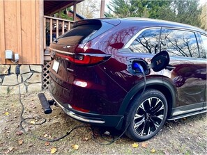 En mørkerød SUV parkeret udendørs med en opladningskabel tilsluttet en ladestation.