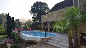 A swimming pool with lounge chairs, a stone building, and a garden with various plants. - Domaine Lacoste (Carsac-Aillac)
