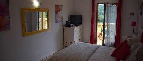 Un dormitorio con cama, cómoda, televisor y balcón con cortinas rojas.