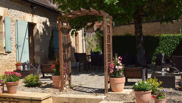A rustic stone building with a wooden pergola, outdoor seating, and potted plants. - Domaine Lacoste (Carsac-Aillac)