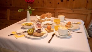 Et morgenbord med forskellig mad, en hvid vase med en rød rose, og en trævæg i baggrunden.