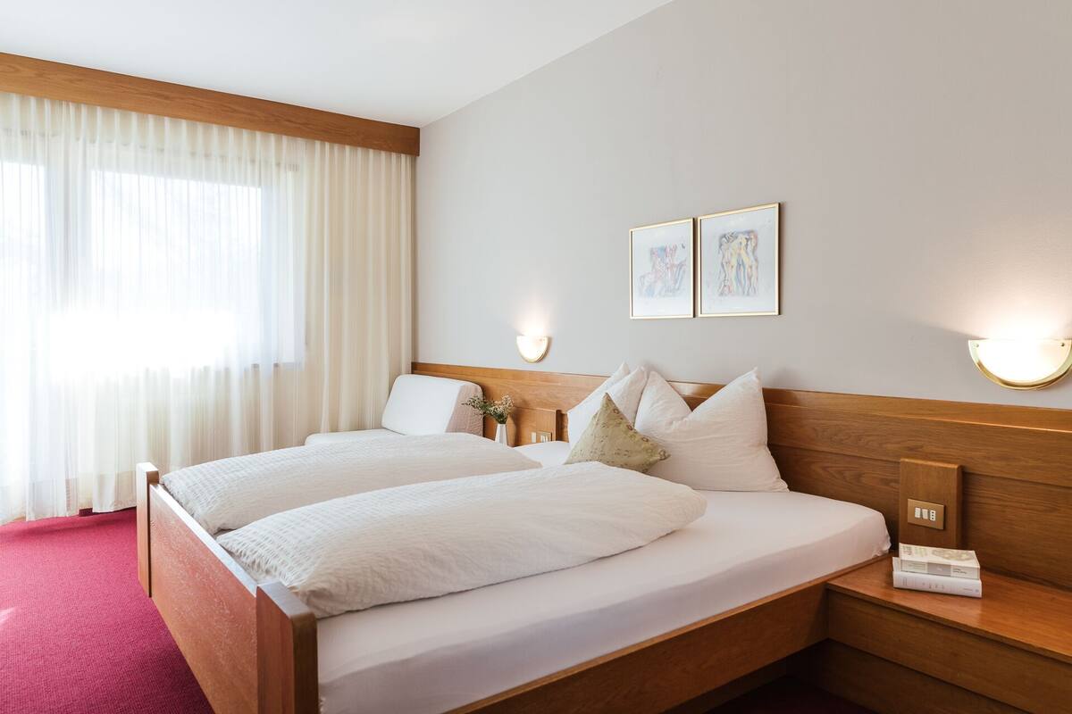 Une chambre d’hôtel avec un lit double, une table de chevet avec une lampe et une fenêtre avec des rideaux légers.
