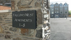 Un mur de pierre sur lequel est apposée une plaque indiquant : « Falcon's Nest Apartments, appartements 1 à 8 ».