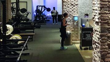 Un gimnasio con equipo de levantamiento de pesas, una pantalla digital y una pared de piedra.