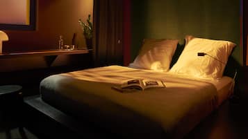 A neatly made bed with pillows and an open book, a bedside table with a lamp, and a small potted plant.