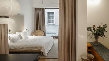 Ein modernes Hotelzimmer mit Bett, Nachttisch, Lampe und Blick ins Freie.
