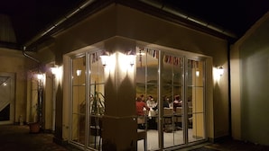 A cozy, well-lit outdoor dining area with a glass enclosure, surrounded by a brick wall and a metal roof. - Ente von Wassertrüdingen (Wassertruedingen)