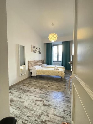 A hotel room with a bed, a mirror, a window with curtains, and a hanging light fixture.