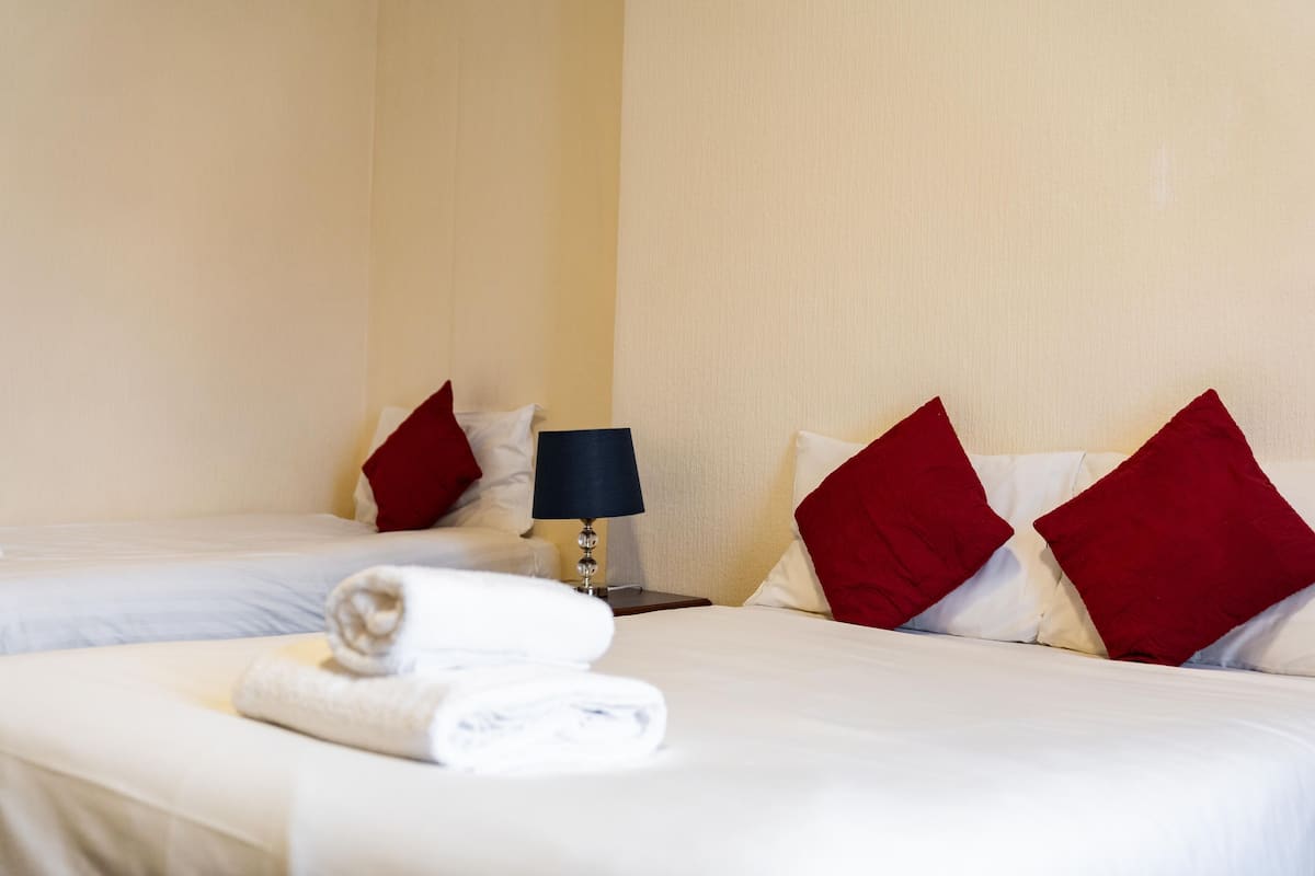 A hotel room with two beds, red and white pillows, a lamp, and folded towels on the beds.