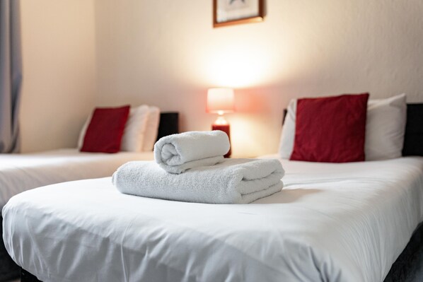 Habitación de hotel con dos camas, ropa de cama blanca, almohadas rojas y una lámpara en la mesita de noche.