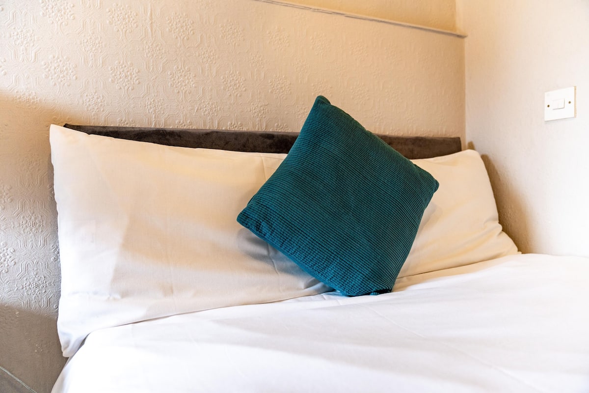 A neatly made bed with white linens and a teal accent pillow.