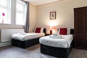 A hotel room with two beds, a radiator, a window with curtains, a nightstand with a lamp, and a wardrobe. - The Royal Hotel Crewe, A BRILLIANT Collection (Crewe)