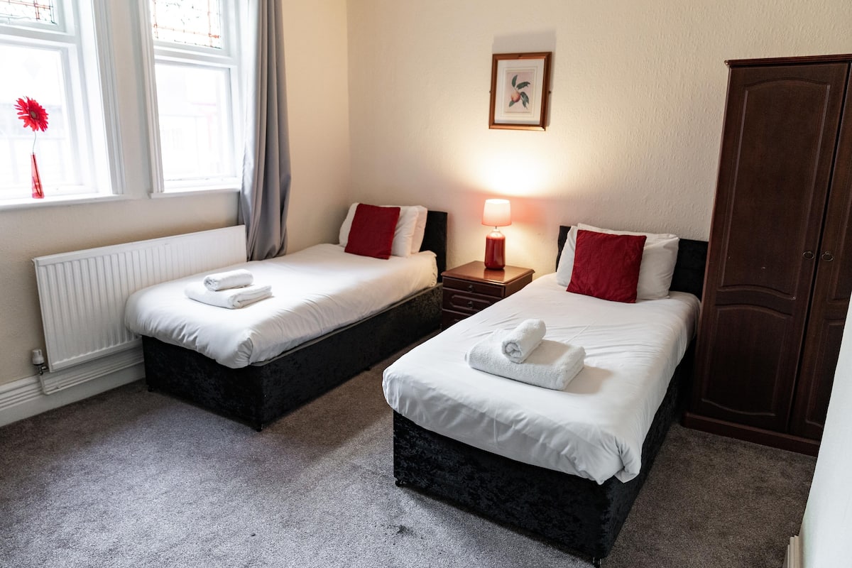 A hotel room with two beds, a radiator, a nightstand with a lamp, a wardrobe, and a framed picture on the wall.