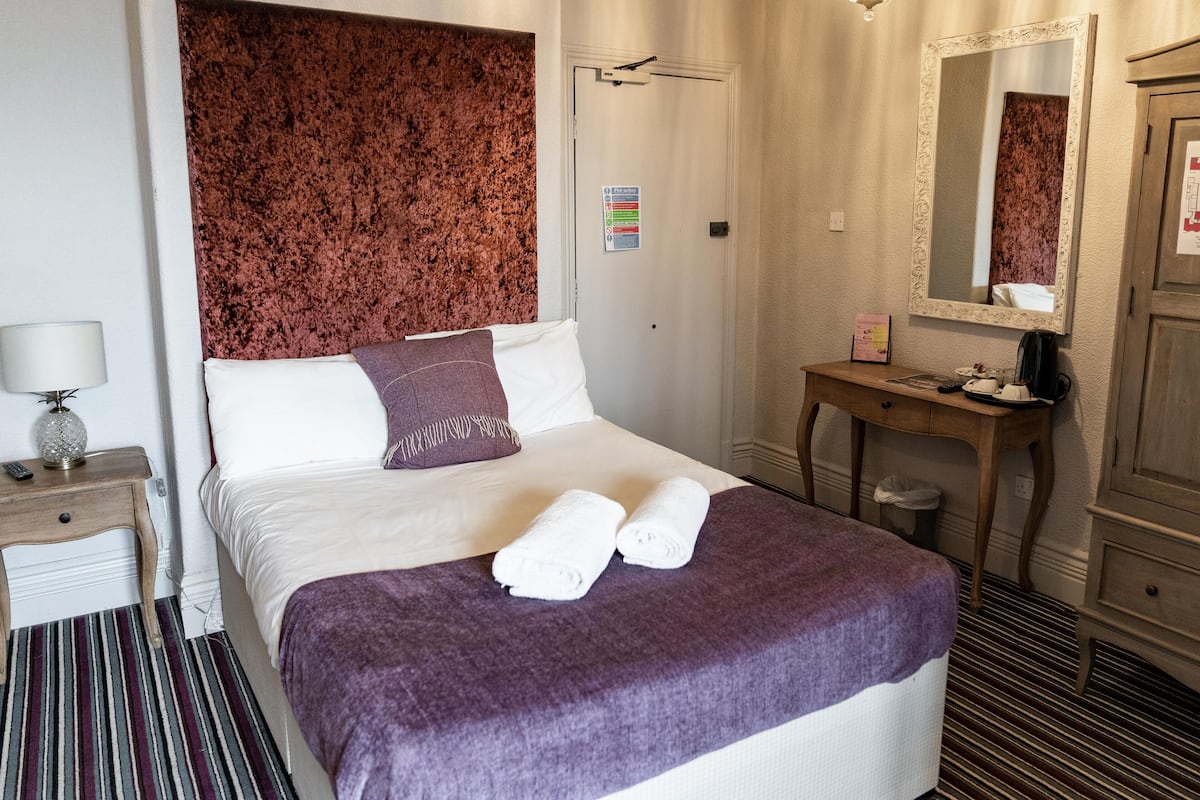 A hotel room with a bed, a bedside table with a lamp, a dresser, and a mirror.