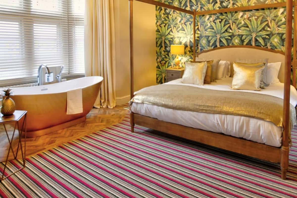 A four-poster bed with a canopy, a freestanding bathtub, and a striped carpet.