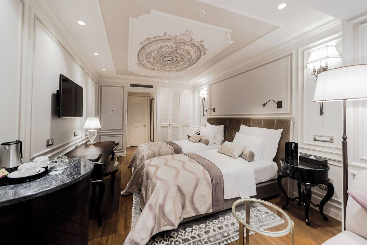 A hotel room with a large bed, a desk with a lamp, a television, and a small table with a lamp.