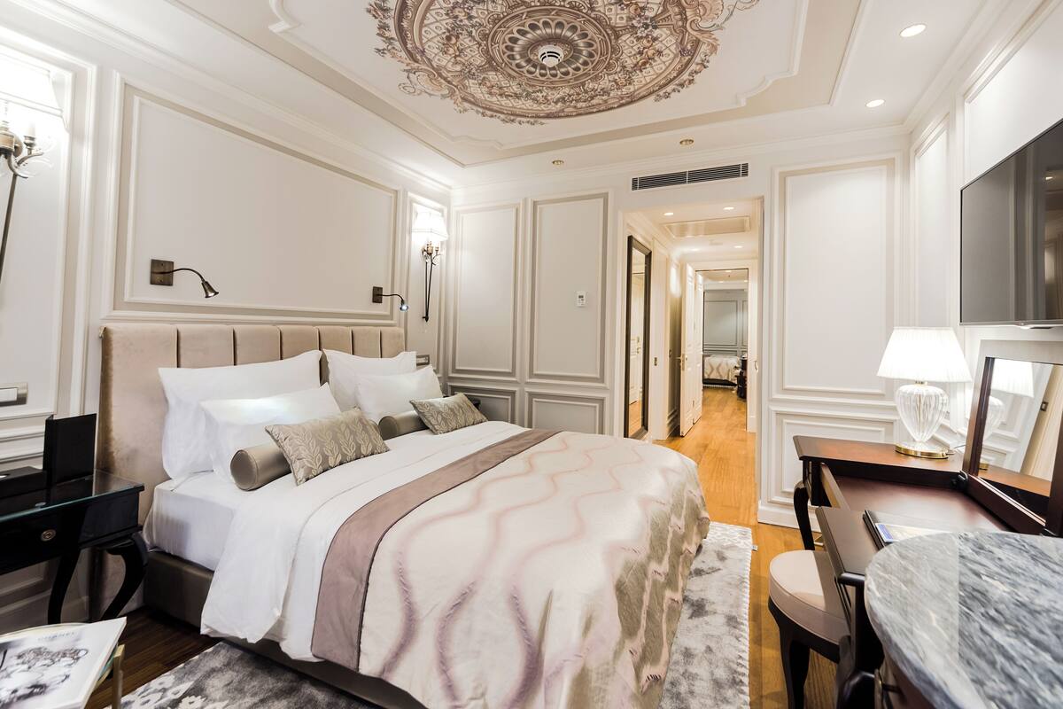 A hotel room with a large bed, a desk, a television, and a decorative ceiling.