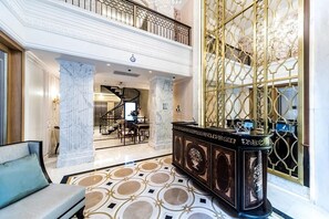 A grand lobby with marble columns, a grand staircase, and a luxurious reception desk.