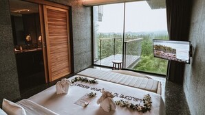 A bedroom with a large bed, a window with a view, a small table, and a TV mounted on the wall. - Varivana Resort Koh Phangan, The Centara Collection (Ko Pha-ngan)