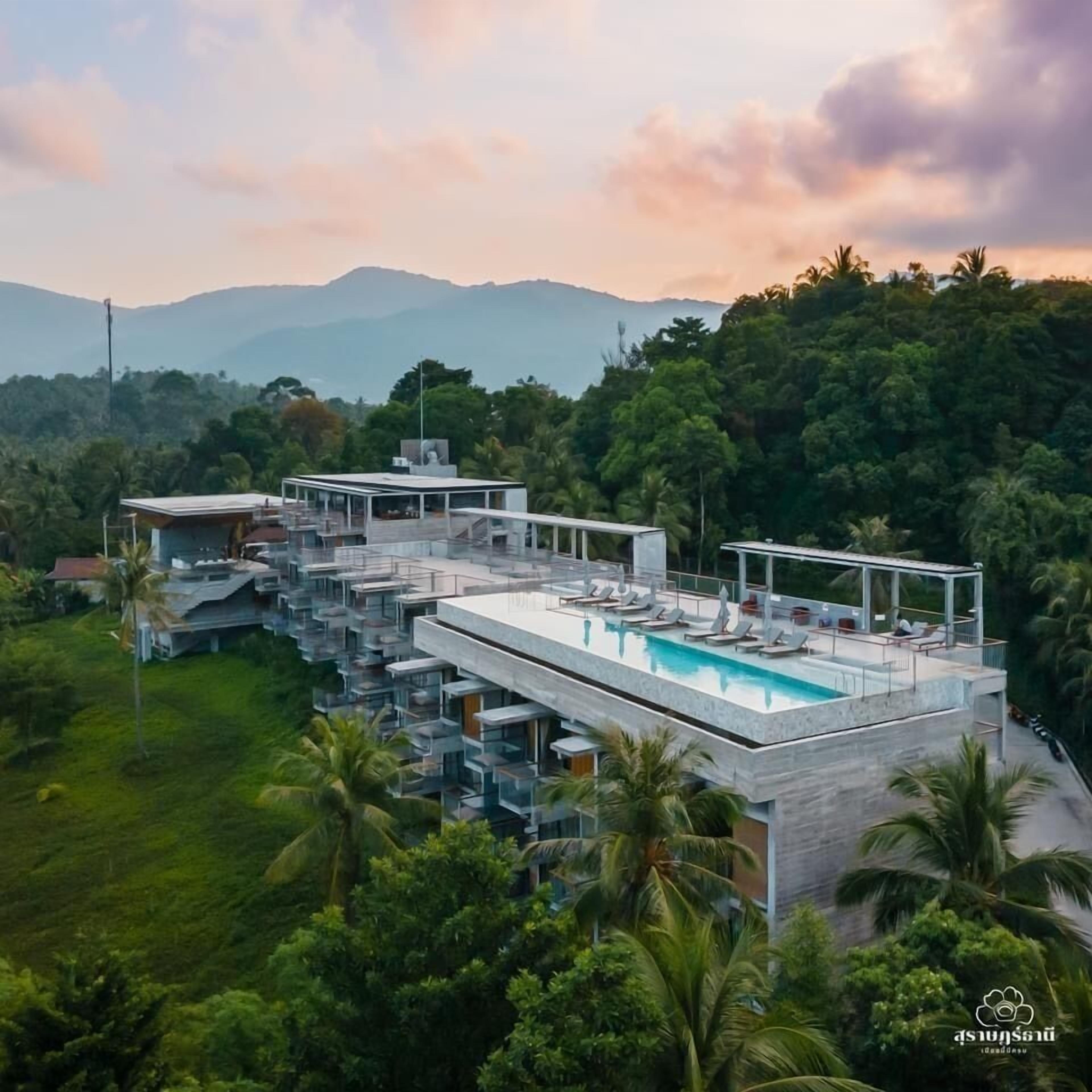 A modern resort with a rooftop pool, multiple balconies, and lush greenery.