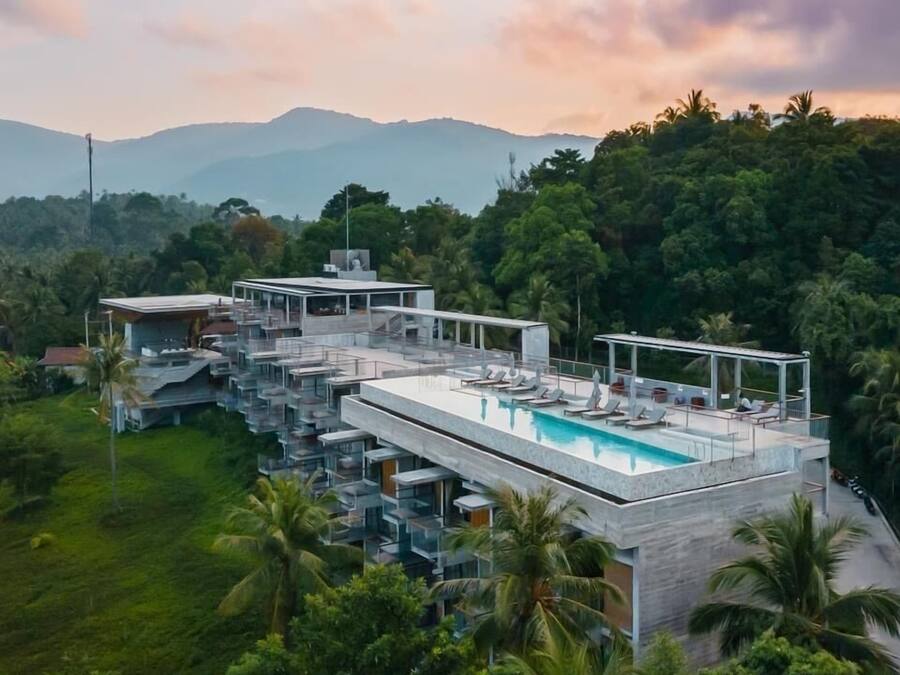 A modern resort with a rooftop pool, multiple balconies, and lush greenery.