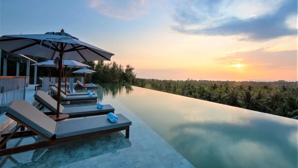 An infinity pool with lounge chairs and umbrellas, surrounded by lush greenery and a sunset view. - Varivana Resort Koh Phangan, The Centara Collection (Ko Pha-ngan)