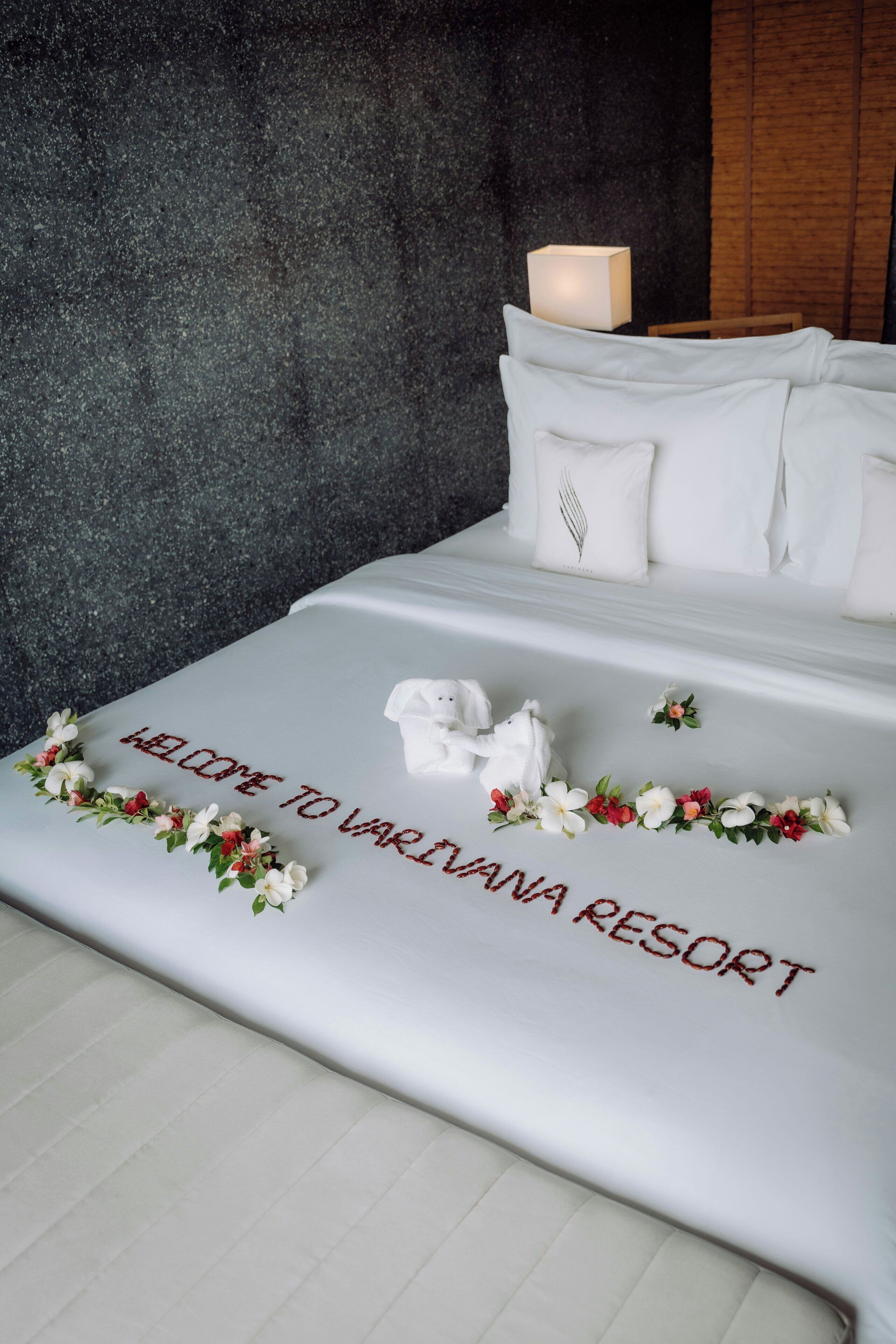 Een net opgemaakt bed met bloemen en de tekst 'WELCOME TO VARIVANA RESORT' op de spreideken.