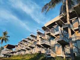 A modern multi-story building with balconies and large windows, surrounded by palm trees.