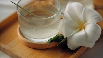 Two glasses of clear liquid on a wooden tray with a white flower beside them.