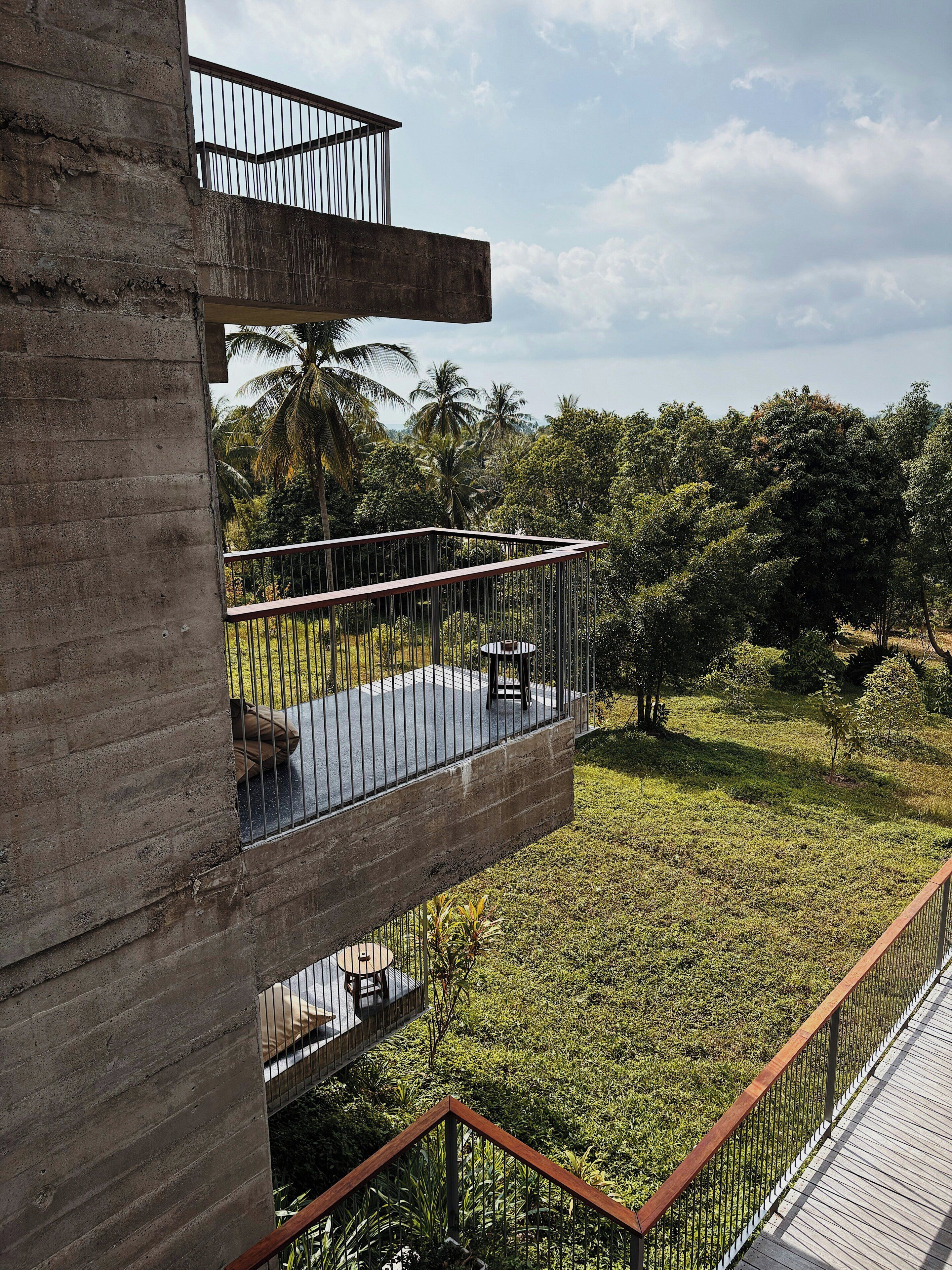 Un balcone all'aperto su più livelli con vista su un giardino rigoglioso e palme.