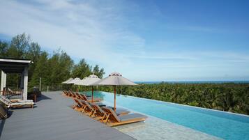 Zona junto a la piscina con sillones reclinables y sombrillas, con vistas a un paisaje exuberante y el océano.
