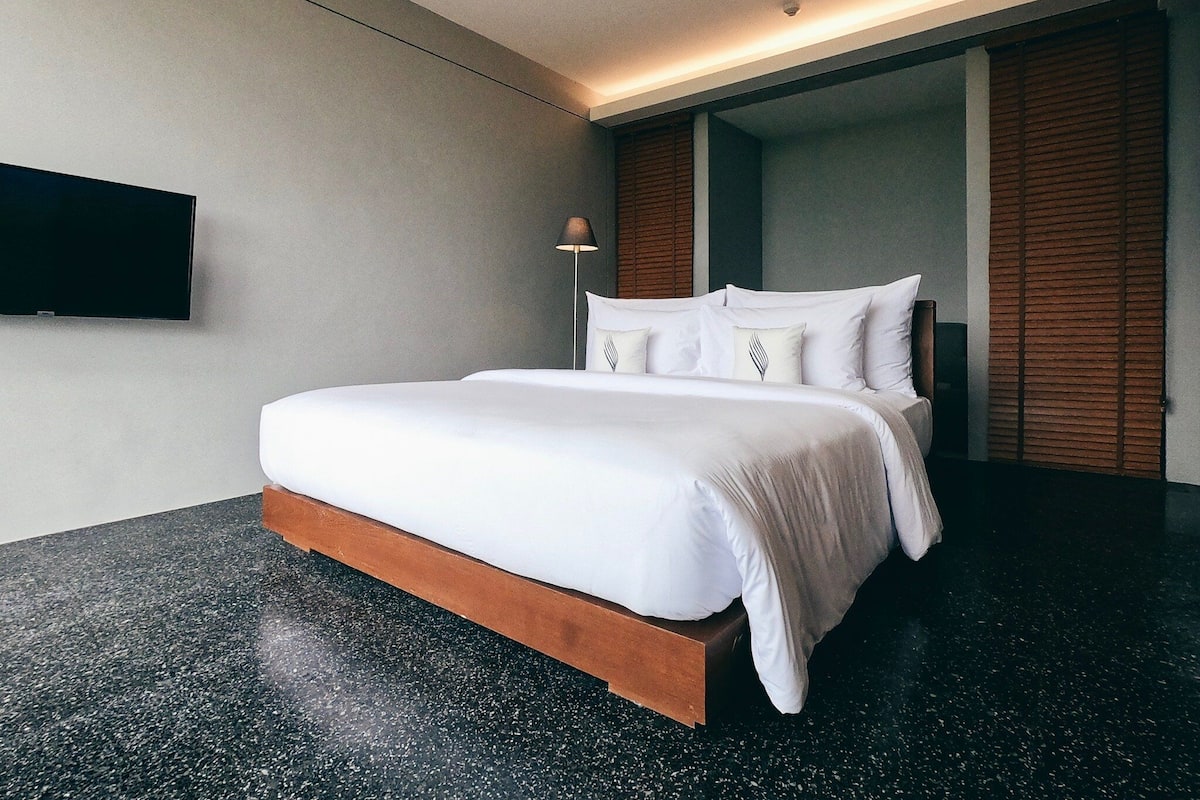 A modern hotel room with a large bed, a flat-screen TV mounted on the wall, and a wooden floor.