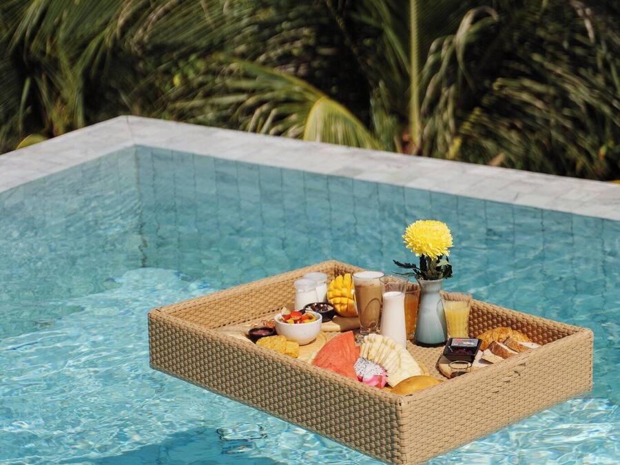 A floating tray with breakfast items in a pool surrounded by palm trees.