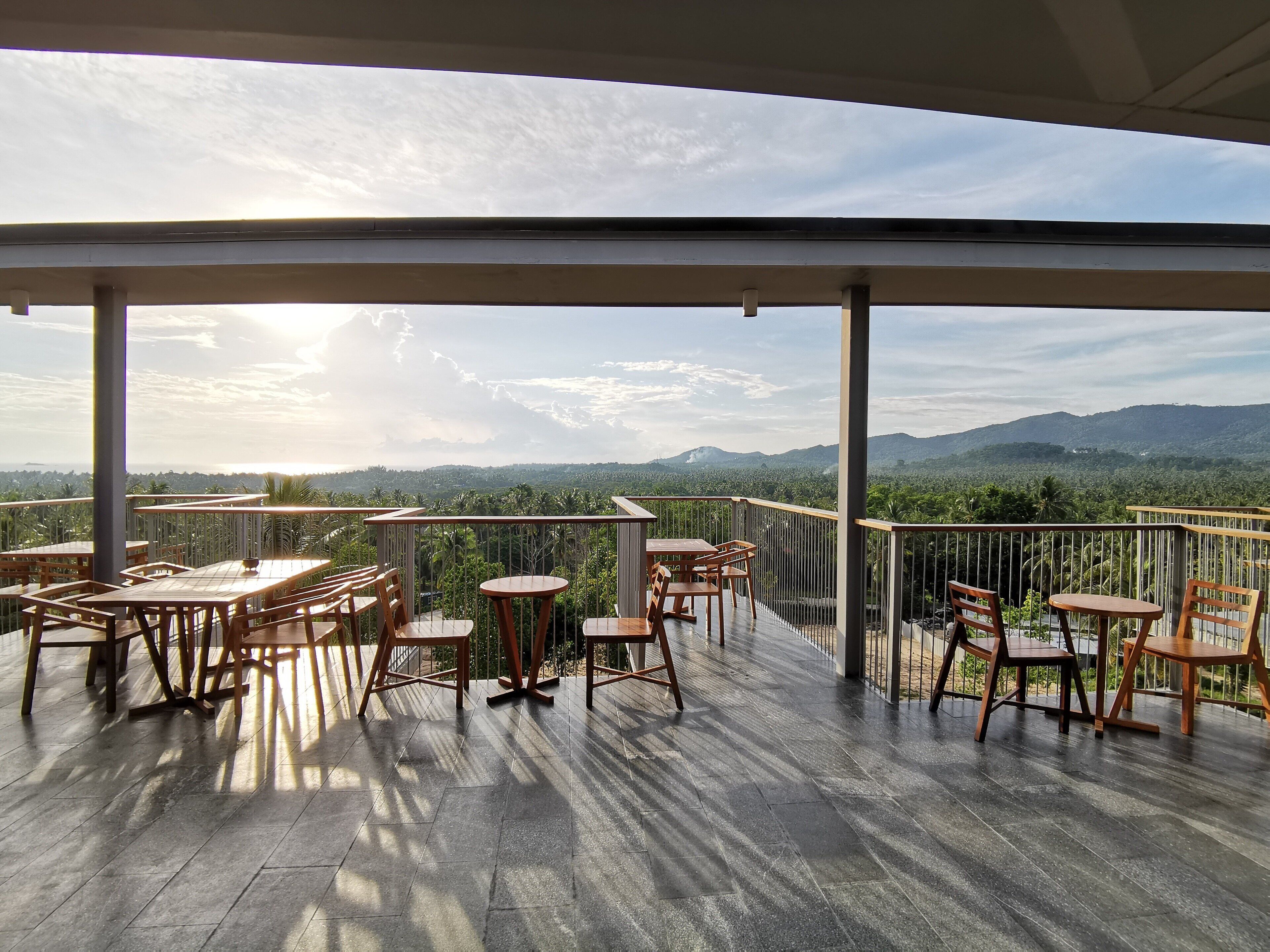 An outdoor terrace with wooden tables and chairs, offering a view of a mountainous landscape.