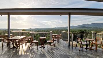 An outdoor terrace with wooden tables and chairs, offering a view of a mountainous landscape.