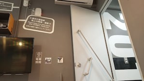 Une chambre d’hôtel dotée d’un grand miroir, d’un climatiseur, d’un ventilateur et d’une affiche indiquant les consignes dans une langue étrangère.