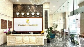 A hotel reception area with a chandelier, marble reception desk, and a glass wall. - Hon Chong Retreat Hotel (Bac Nha Trang)