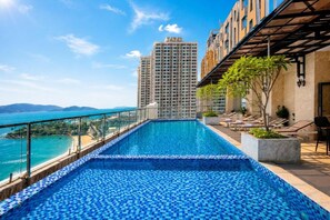 A rooftop pool with a view of the sea and a tall building in the background.