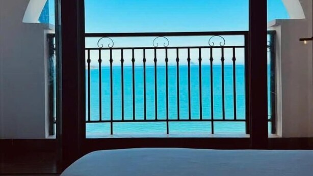 A room with a bed, a view of the sea through a balcony with a railing, and a large arched window. - Hon Chong Retreat Hotel (Bac Nha Trang)