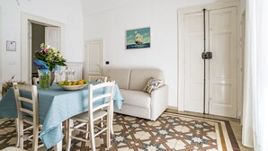 A dining area with a table set for two, a vase with flowers, and a painting of a sailboat on the wall. - Domus Neptuni (Monopoli)