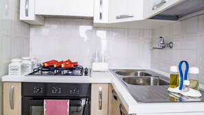 A compact kitchen with white cabinets, a gas stove, a built-in oven, and a stainless steel sink. - Domus Neptuni (Monopoli)