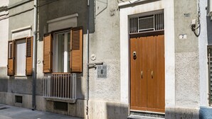 A building with a wooden door and shutters, a small balcony, and a number sign indicating the address. - Domus Neptuni (Monopoli)