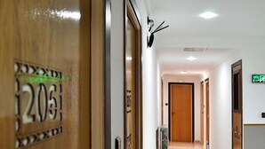 A hotel hallway with a wooden door labeled "205", a radiator, and a corridor leading to another room.