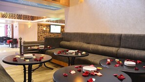 A hotel lobby with a sofa, round tables, and a TV screen.