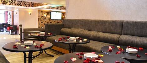 A hotel lobby with a sofa, round tables, and a TV screen.