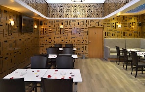 A restaurant with a modern interior, featuring patterned walls, a wooden ceiling, and a mix of dining tables and booths. - Hotel PALACE (Meknes)