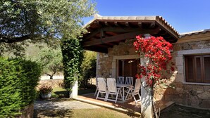 A stone building with a covered patio, outdoor seating, and a potted plant with red flowers. - Residenza Lu Fraili (San Teodoro)